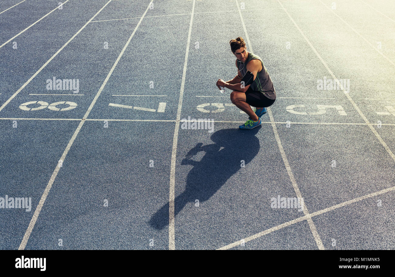Athleten sitzen auf der Laufstrecke mit einer Flasche Wasser in der Hand. Läufer an der Startlinie tragen Kopfhörer und Handy in Arm band. Stockfoto