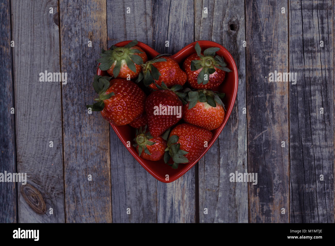 Herzförmige Schale voller Frische Erdbeeren auf vintage Holz- Hintergrund. Flach, Ansicht von oben. Stockfoto