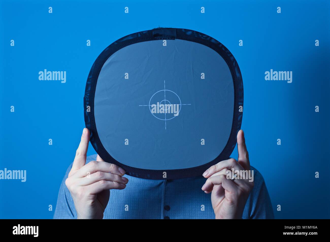 Mann hält 18% graue Karte vor seinem Gesicht bereit für ein Portrait schießen, mit einem blauen Hintergrund Stockfoto