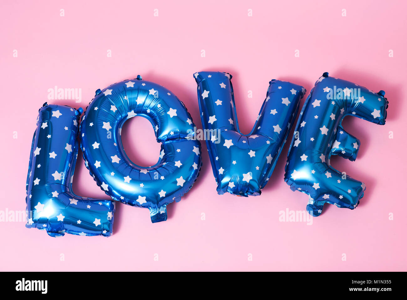 Einige blauen Brief - geformte Ballons mit weißen Sternen bilden das Wort Liebe gegen einen rosa Hintergrund gemusterten Stockfoto