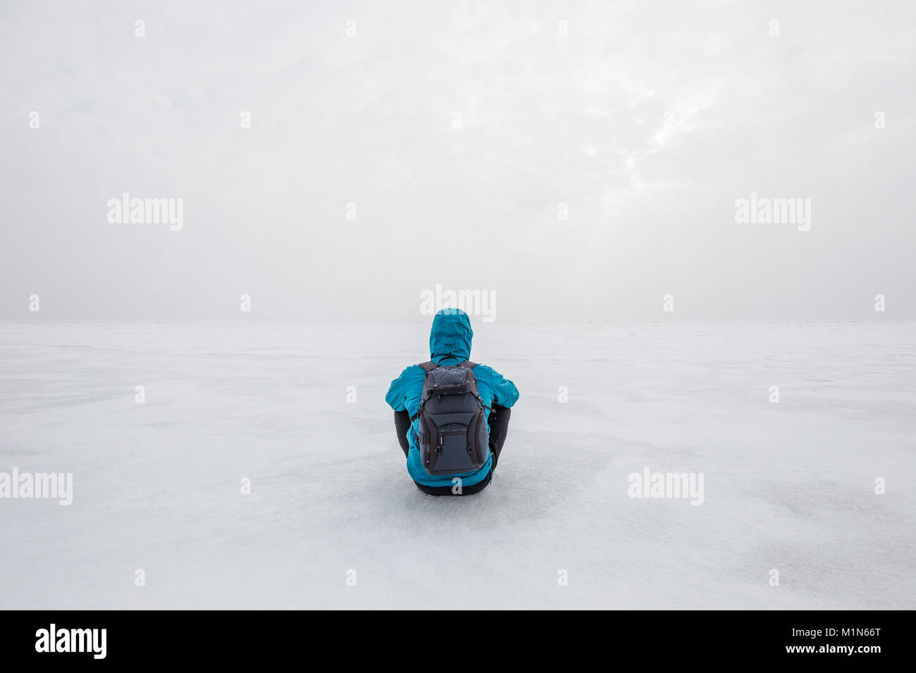 Mann mit Rucksack saß alleine auf dem See Eis und nach vorne starrte. Kalte Winter Tag bewölkt Stockfoto