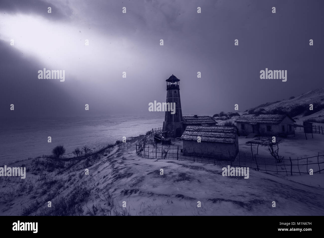 Alten hölzernen Leuchtturm in der Nacht am Rand des gefrorenen Hafen mit bewölktem Himmel. Blau stimmungsvolles Licht Stockfoto