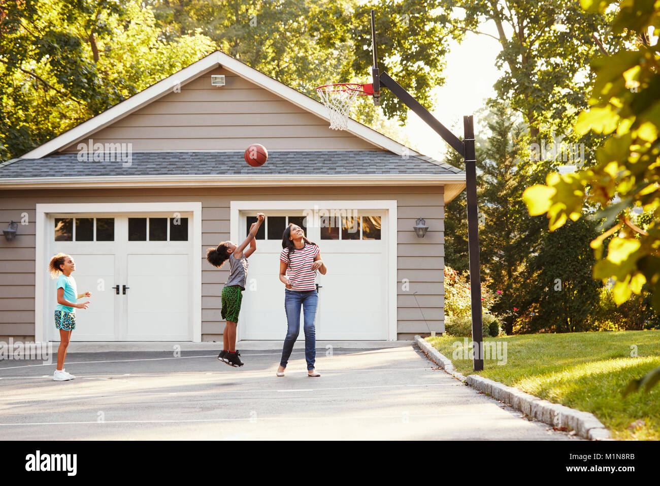 Mutter und Kinder Basketball spielen in der Einfahrt zu Hause Stockfoto