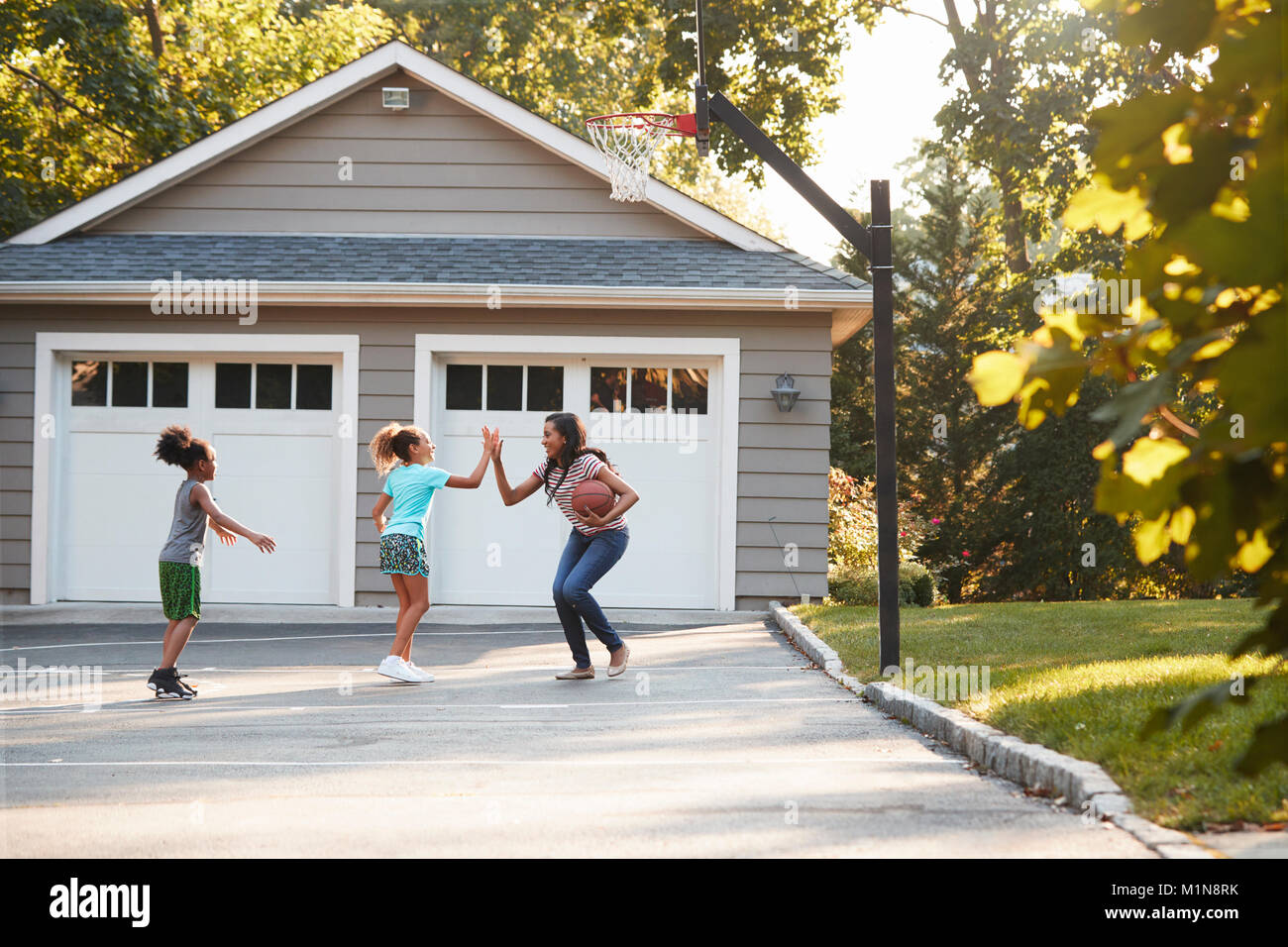 Mutter und Kinder Basketball spielen in der Einfahrt zu Hause Stockfoto