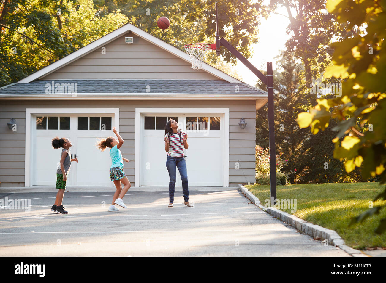Mutter und Kinder Basketball spielen in der Einfahrt zu Hause Stockfoto