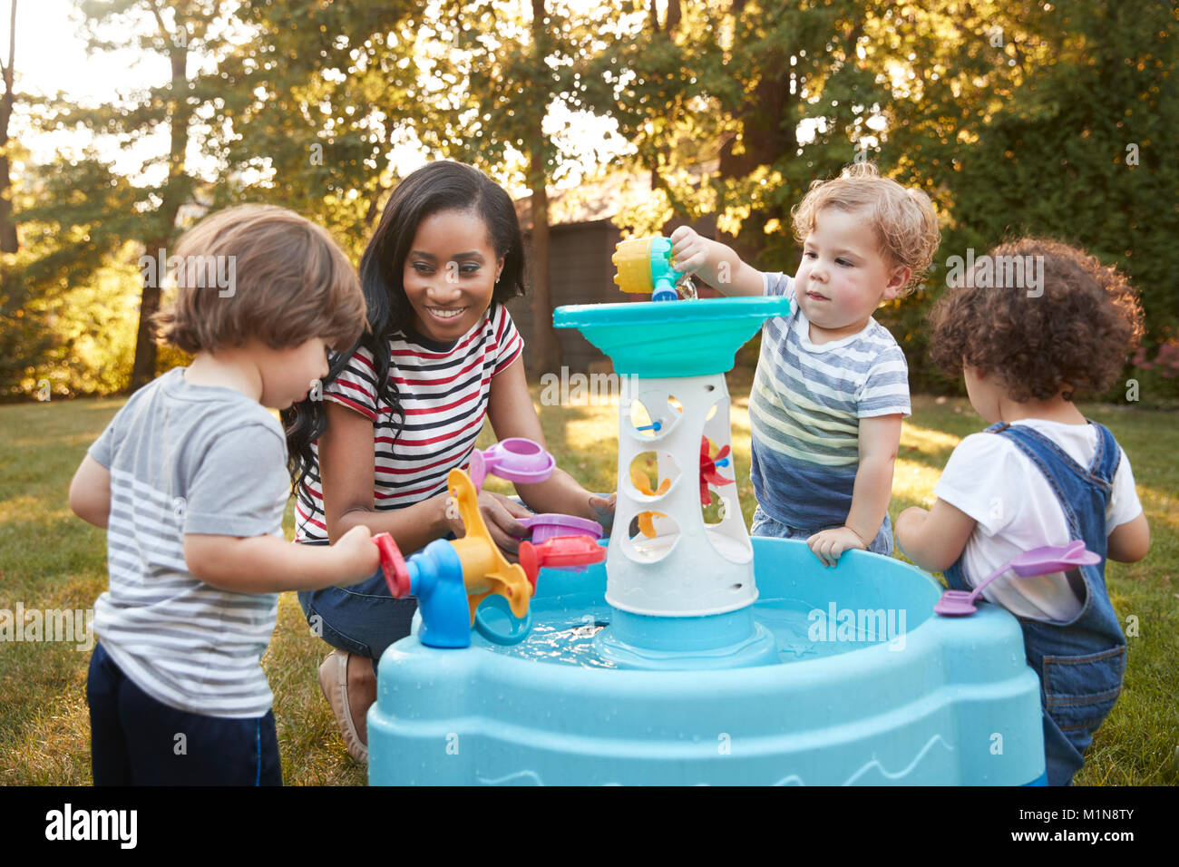 Mutter und Kinder spielen mit Wasser im Garten Stockfoto