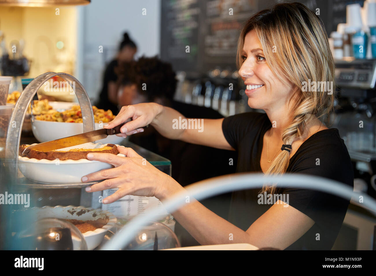 Kellnerin hinter Zähler in Coffee Shop Schneiden Stück Kuchen Stockfoto