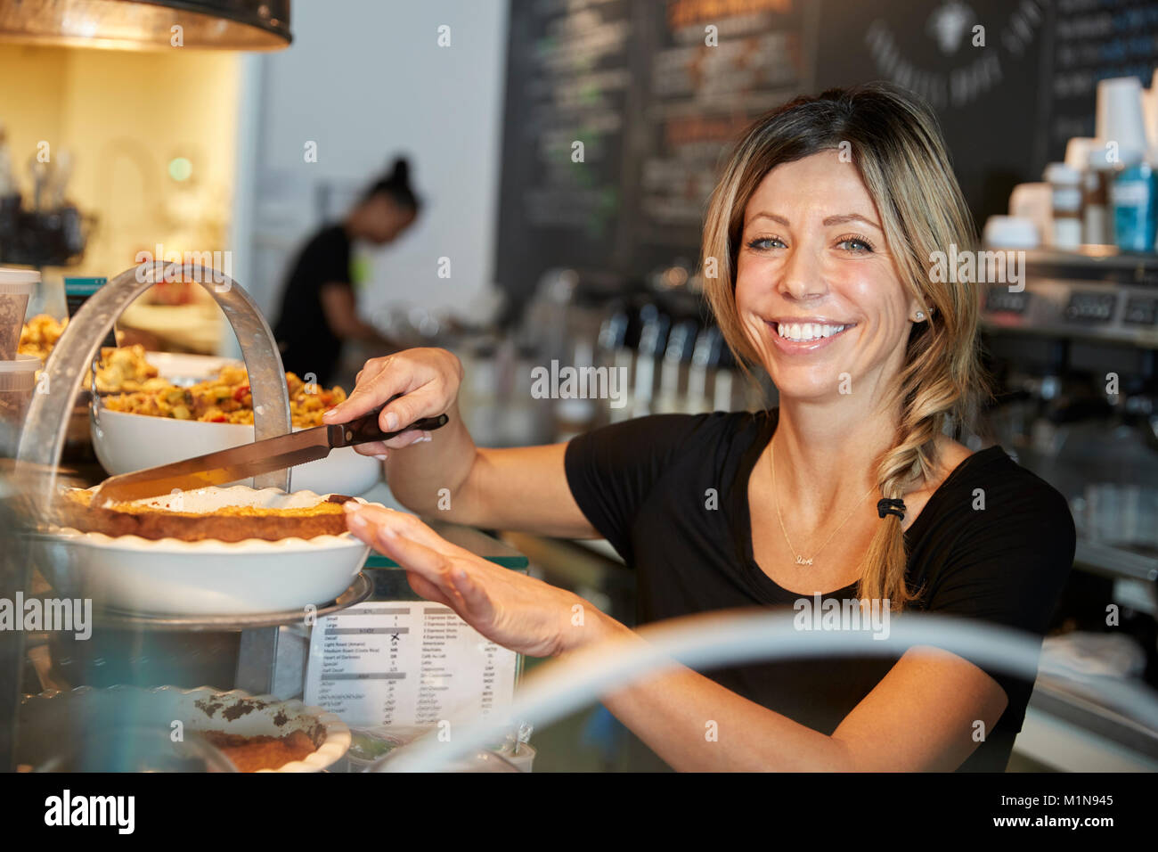 Kellnerin hinter Zähler in Coffee Shop Schneiden Stück Kuchen Stockfoto