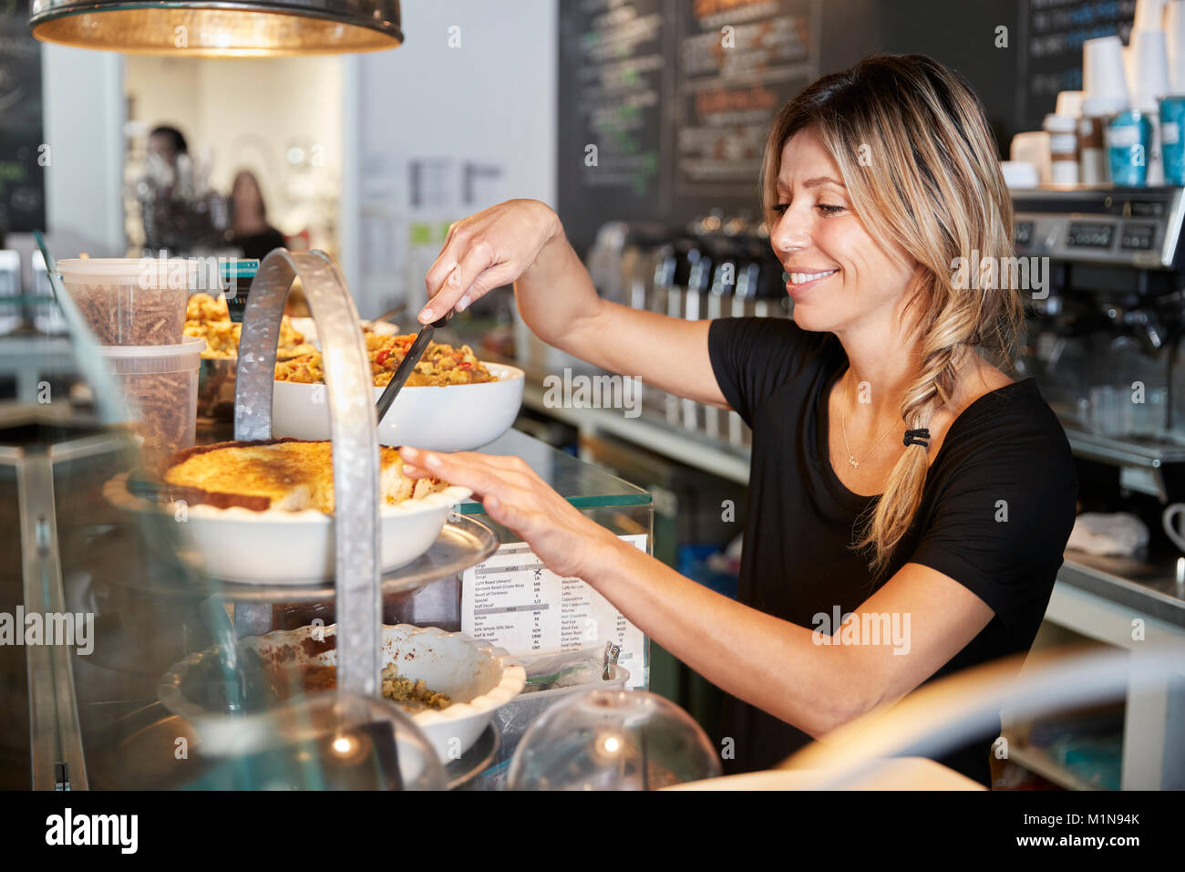 Kellnerin hinter Zähler in Coffee Shop Schneiden Stück Kuchen Stockfoto