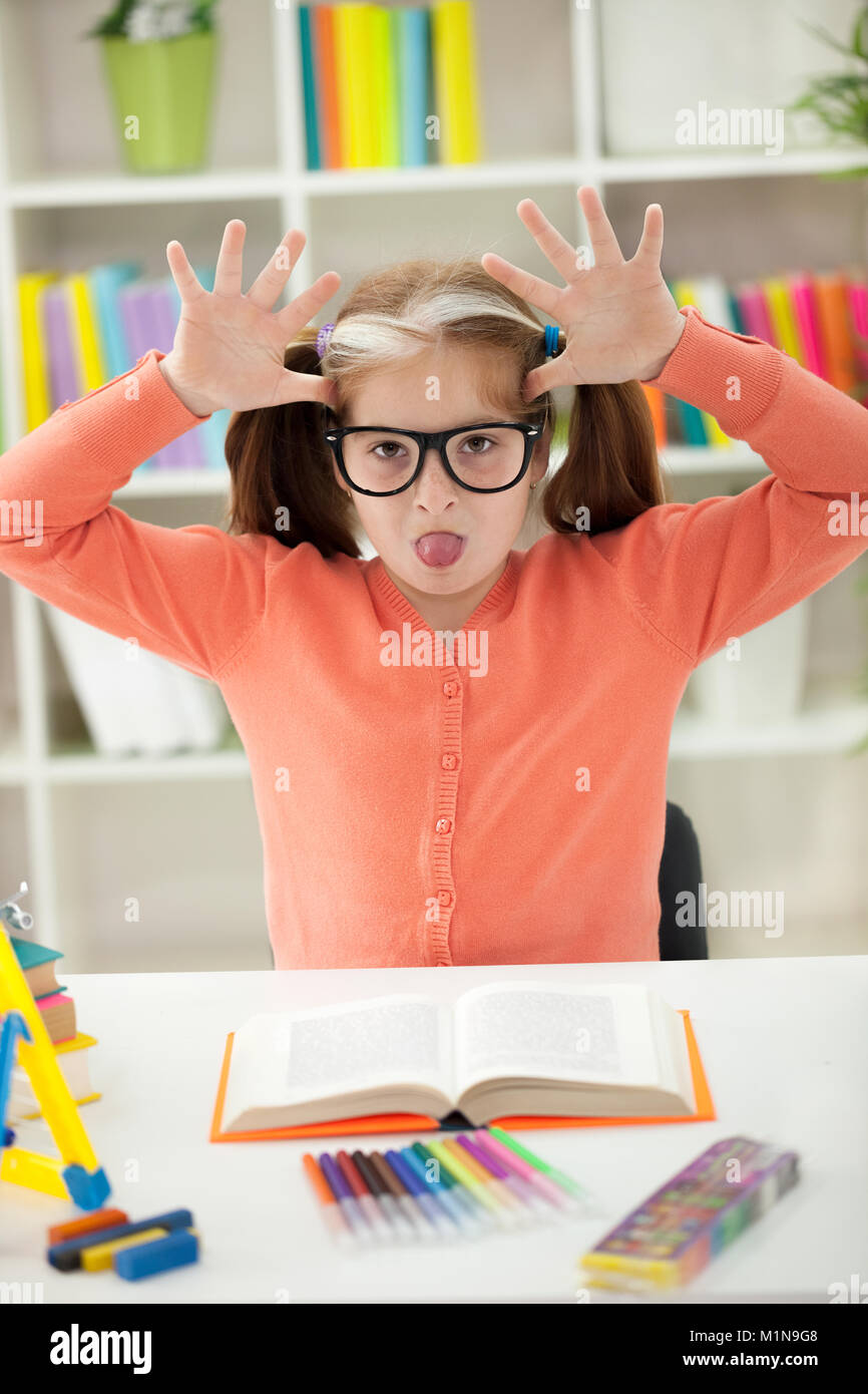 Süß lustiges kleines Mädchen hält Hausaufgaben lesen ihre Zunge heraus zu haften Stockfoto