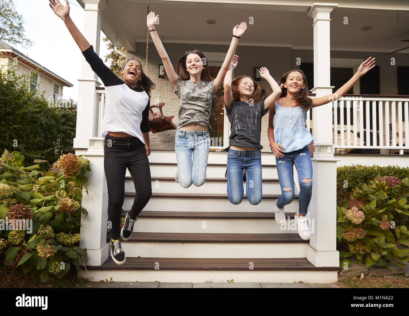Vier junge jugendlich Mädchen Sprung vom vorderen Stufen eines Hauses Stockfoto