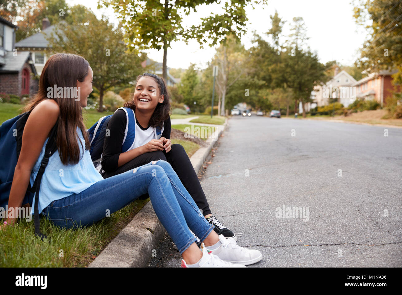 Zwei jugendlich Freundinnen Sitzen sprechen am Straßenrand Stockfoto
