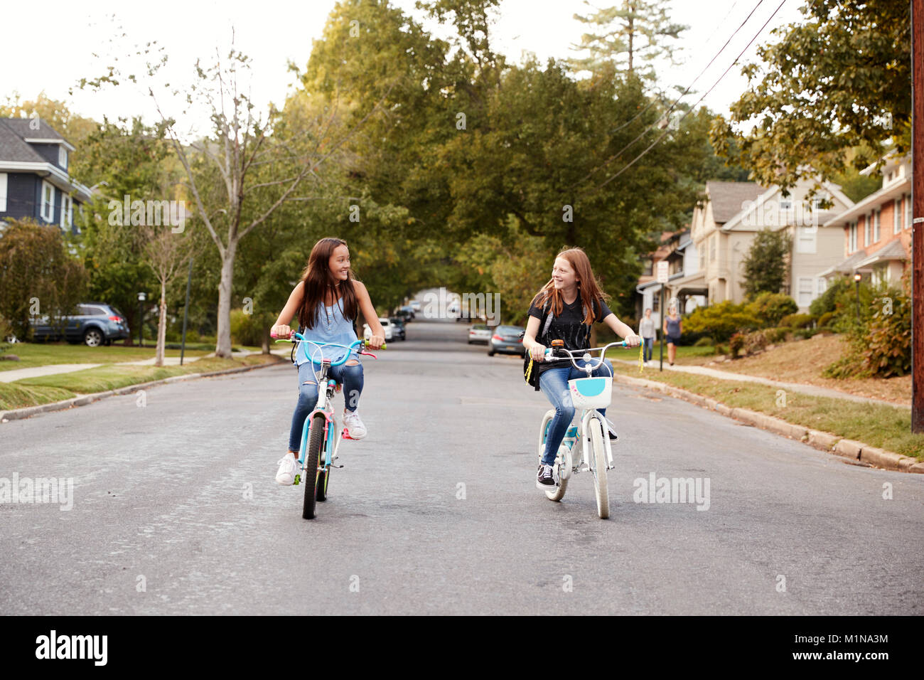 Zwei jugendlich Mädchen reiten Fahrräder in einer ruhigen Straße, Vorderansicht Stockfoto