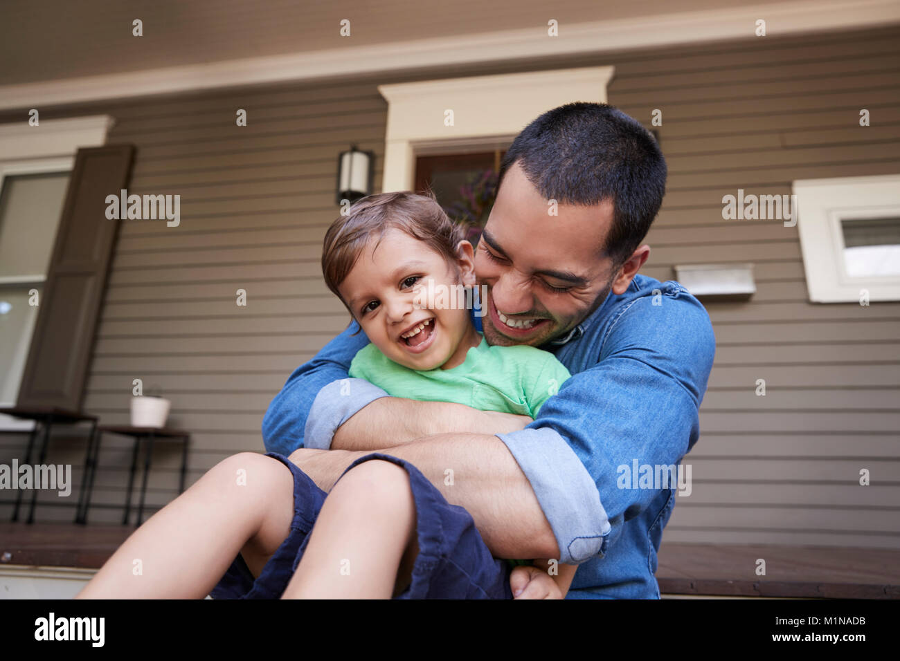 Vater umarmt Sohn als Sie sitzen auf der Veranda des Hauses zusammen Stockfoto