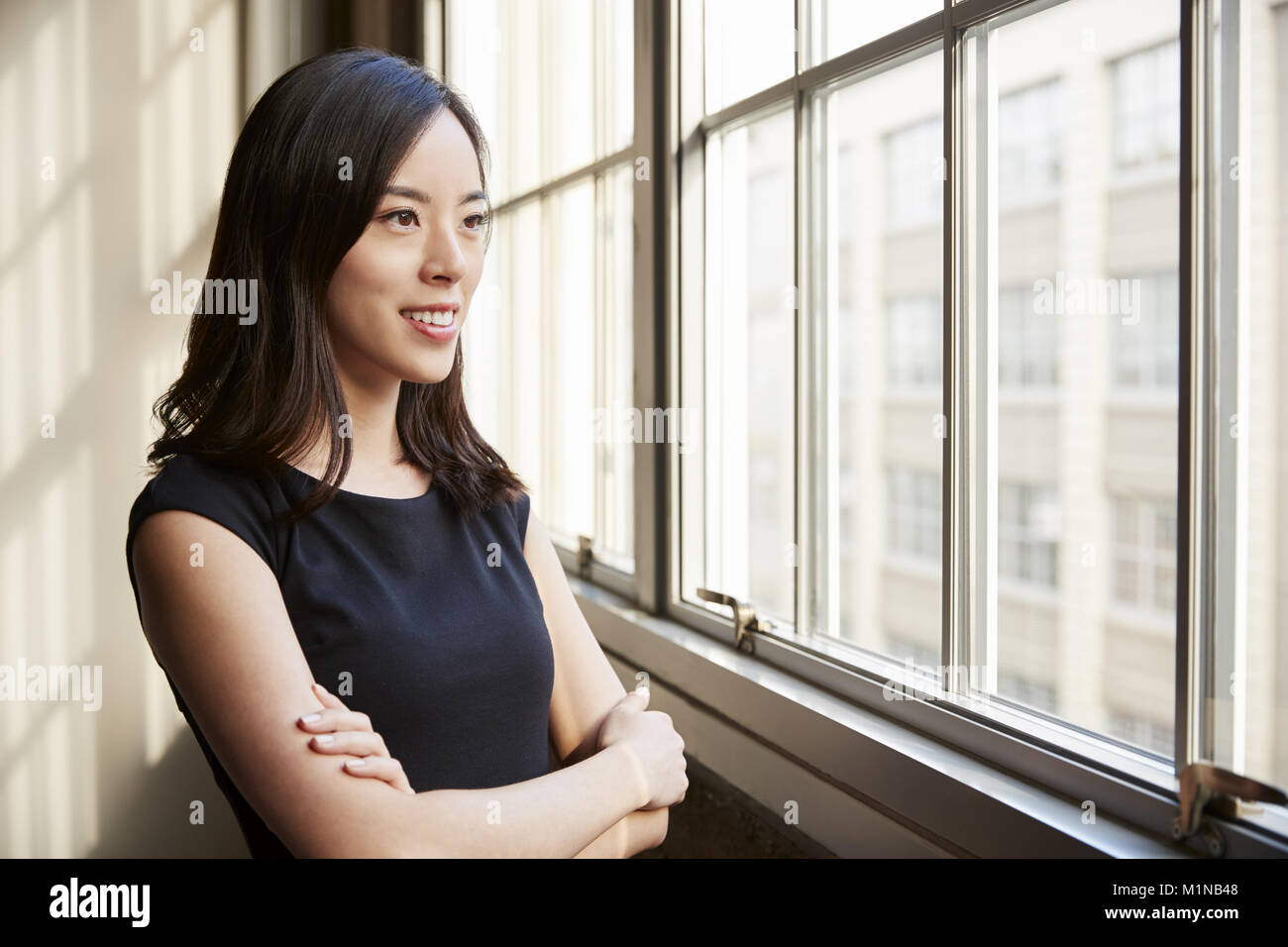 Lächelnde junge chinesische Geschäftsfrau Blick aus Fenster Stockfoto