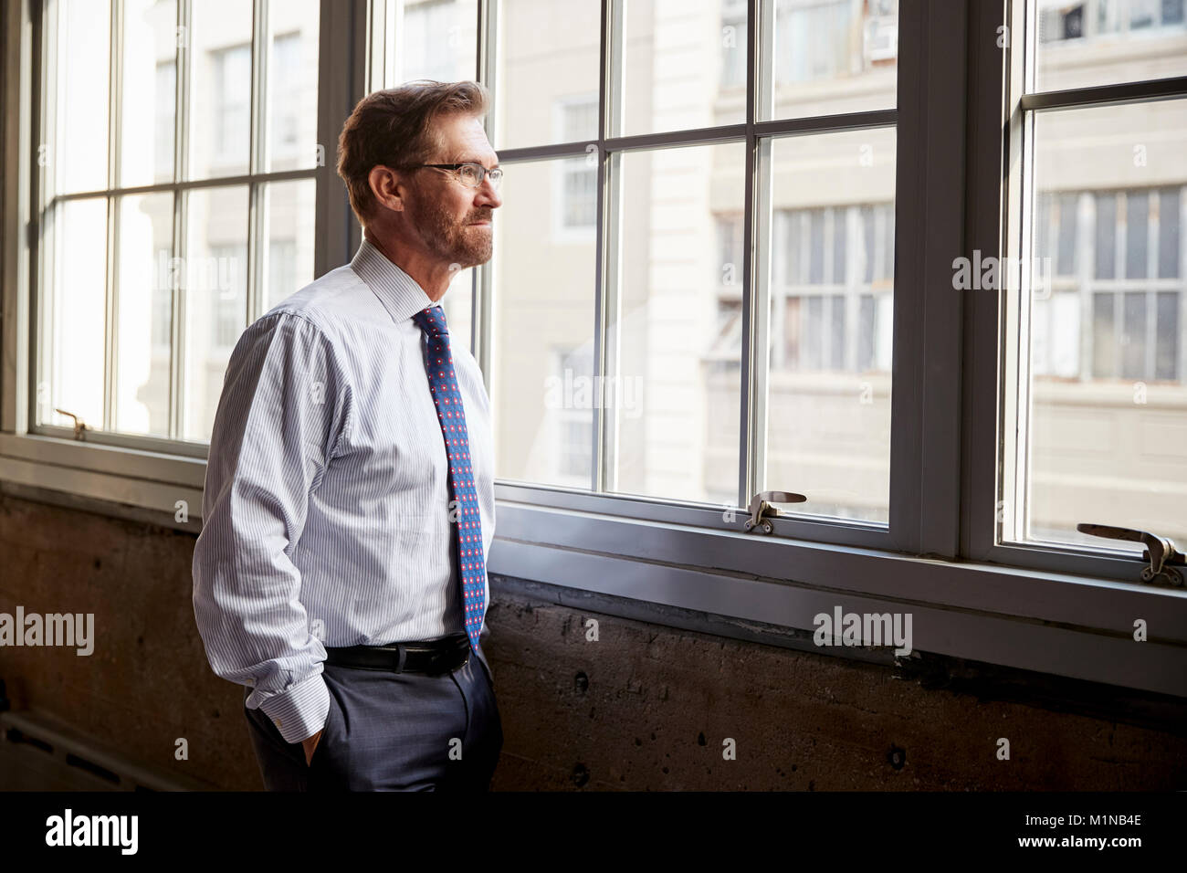 Senior Geschäftsmann Blick aus Fenster, Hände in den Taschen Stockfoto