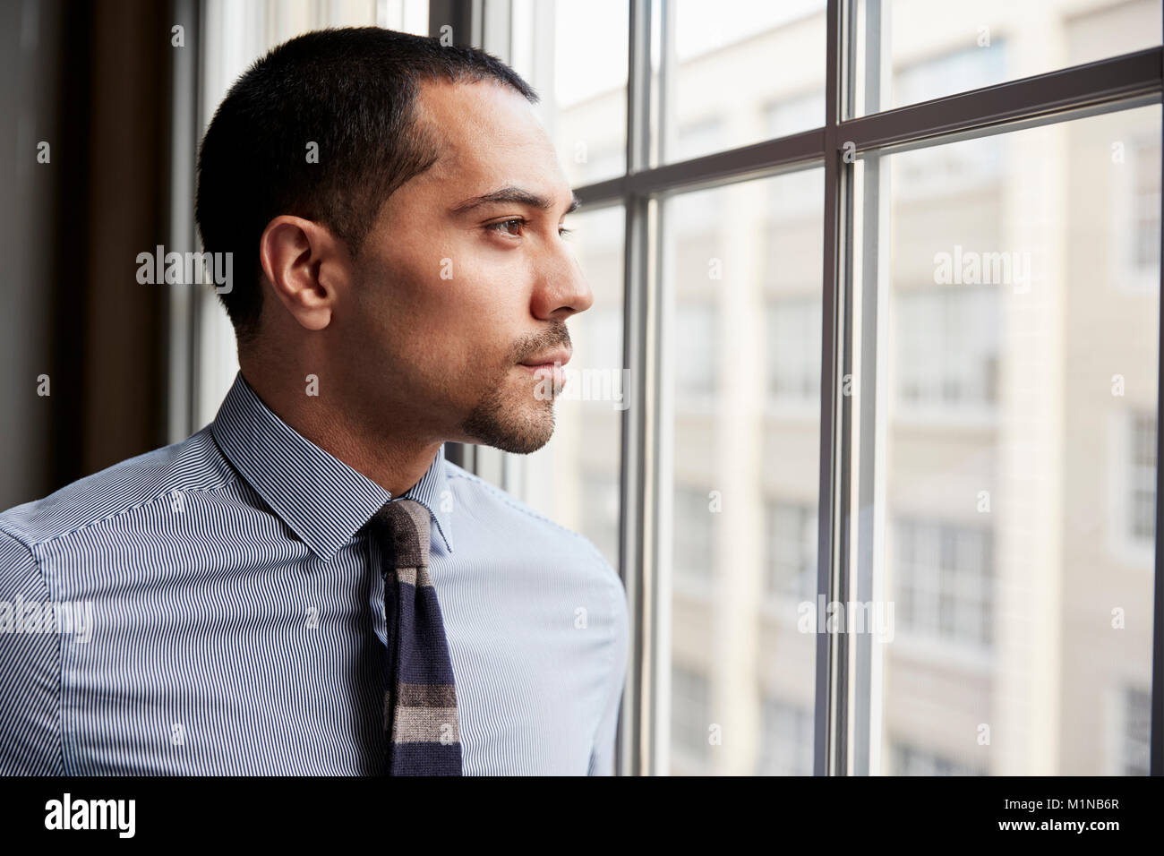 Junge Hispanic Mann Blick aus Fenster Stockfoto