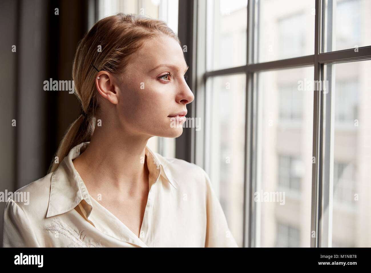 Blonde junge geschäftsfrau Blick aus Fenster Stockfoto