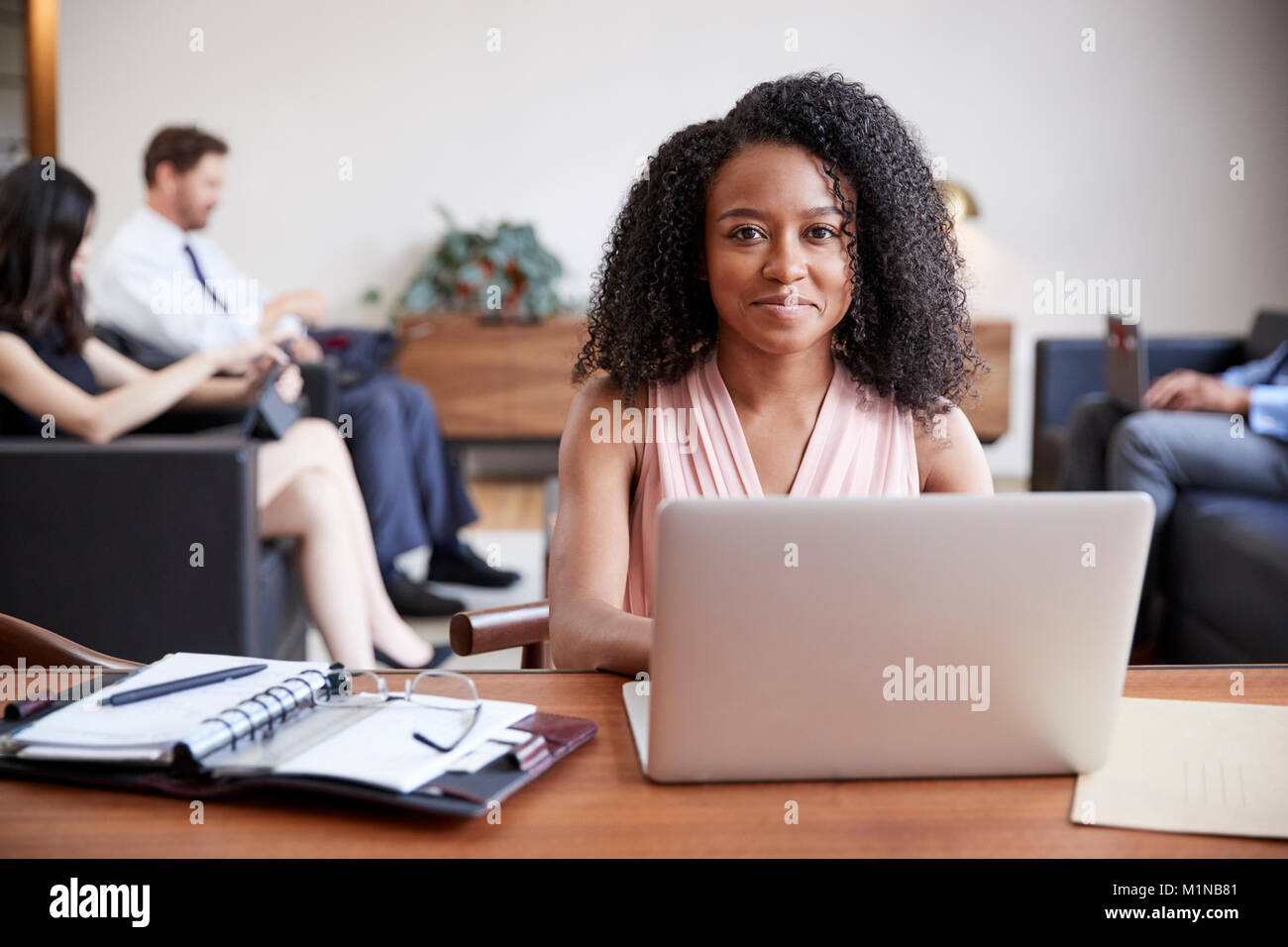 Junge schwarze Geschäftsfrau, die an einem Schreibtisch arbeiten blickt in die Kamera Stockfoto