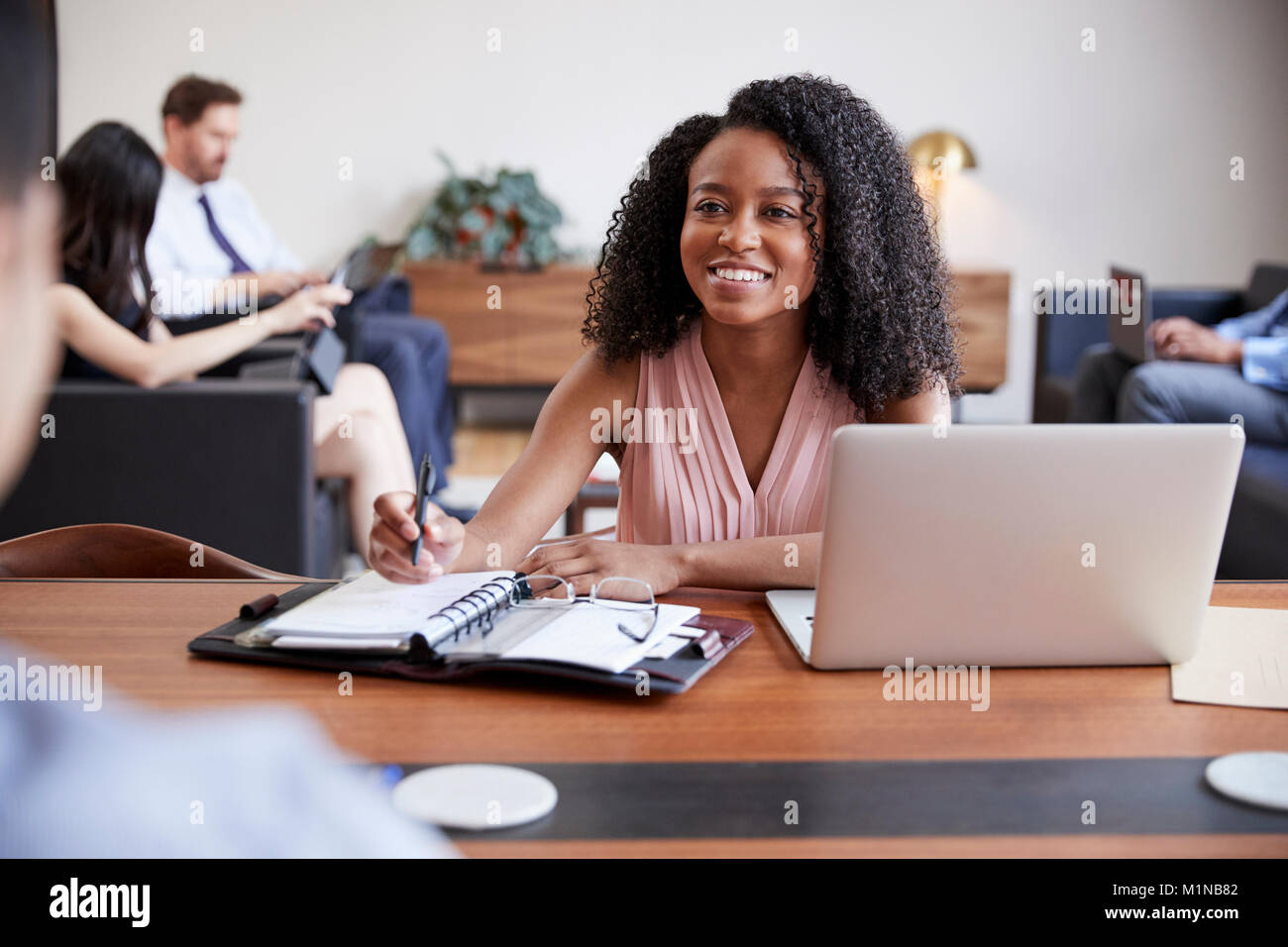 Junge schwarze Frau am Schreibtisch auf der Suche nach einem Kollegen gegenüber Stockfoto