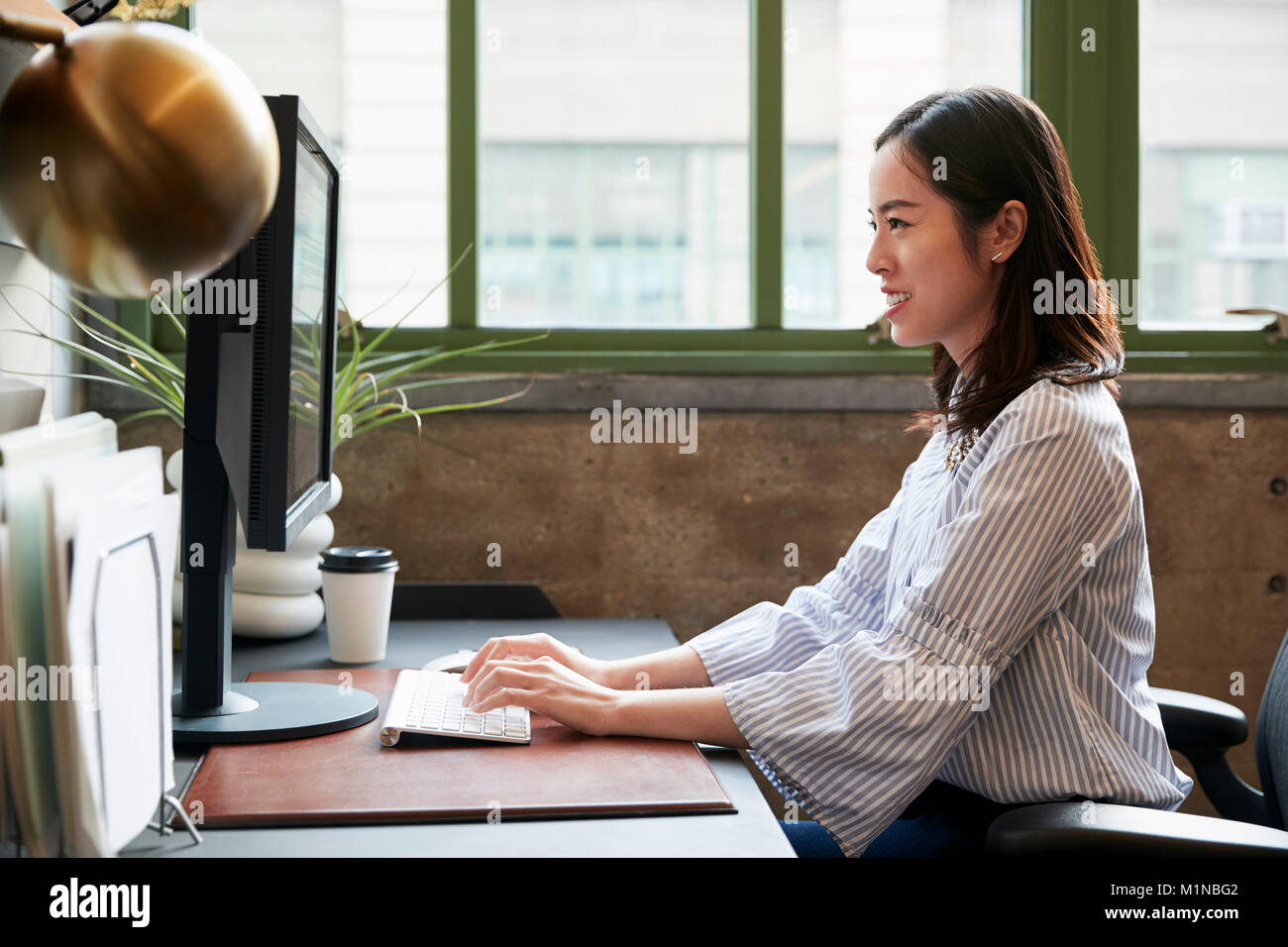 Chinesische Frau an einem Computer in einem Büro arbeiten, Seitenansicht Stockfoto