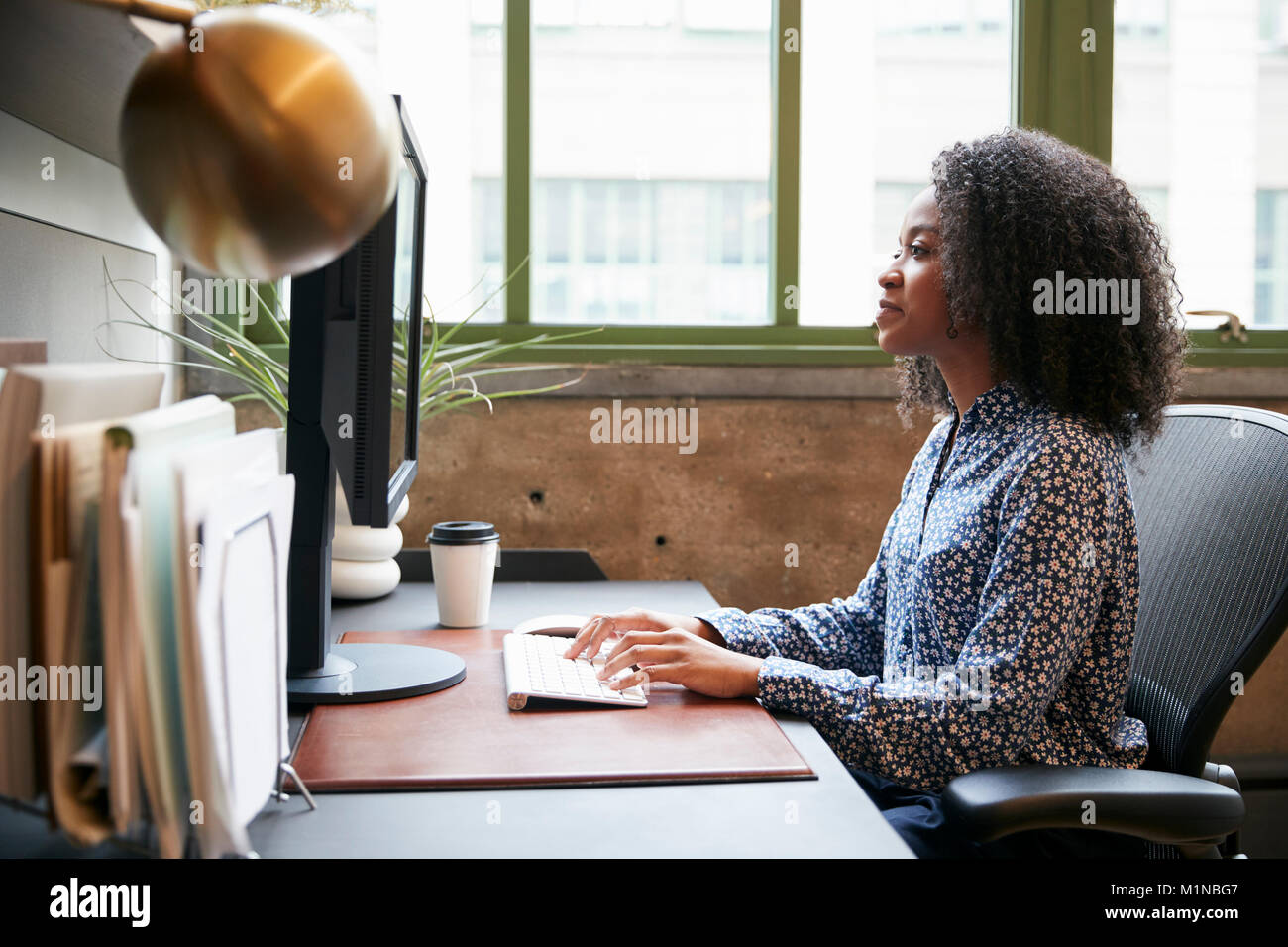 Schwarze Frau an einem Computer in einem Büro arbeiten, Seitenansicht Stockfoto