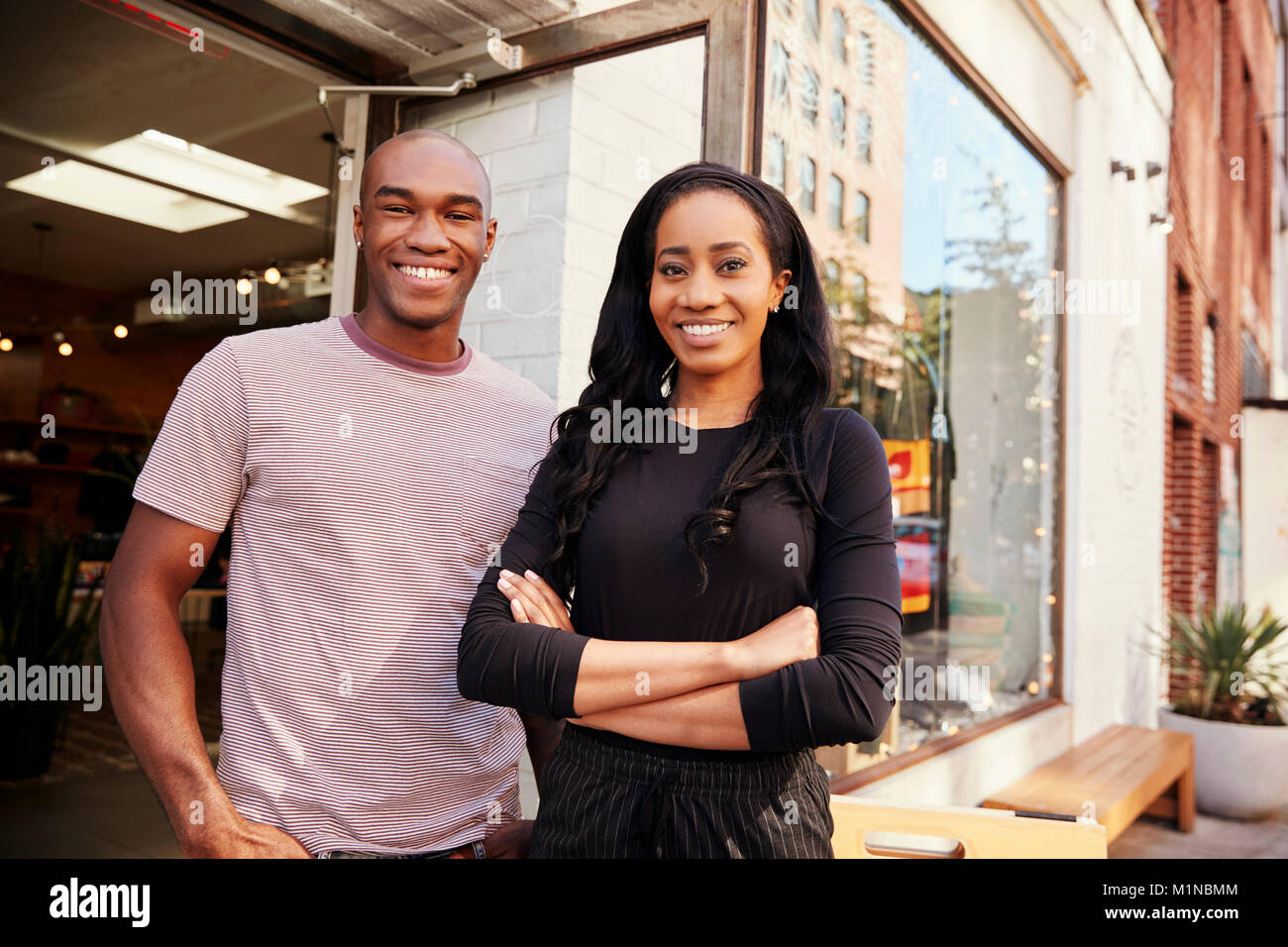 Junges Paar lächelnde Kamera außerhalb ihrer Kleidung Shop Stockfoto