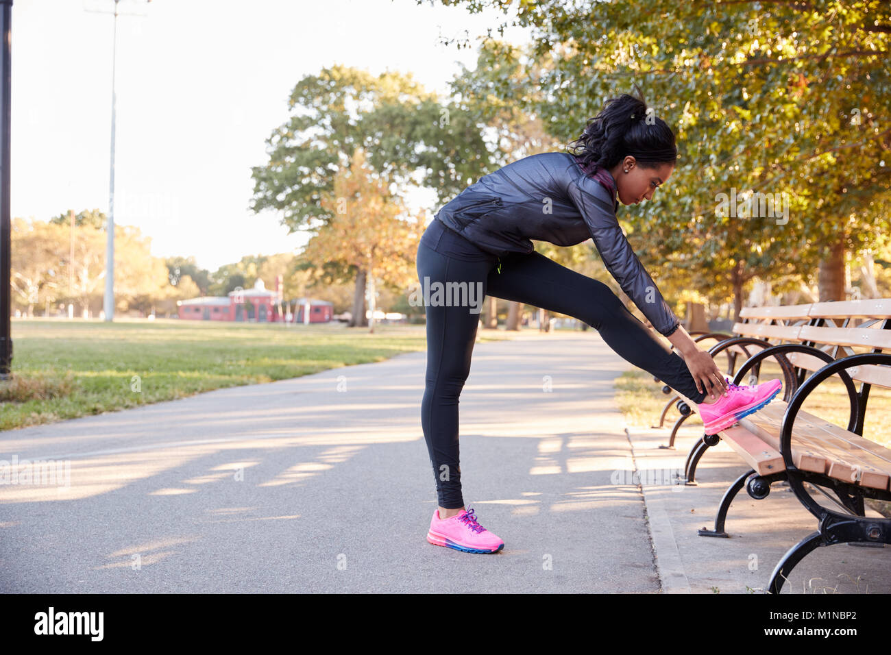 Junge schwarze Frau, die sich auf Bank in einem Park, volle Länge Stockfoto