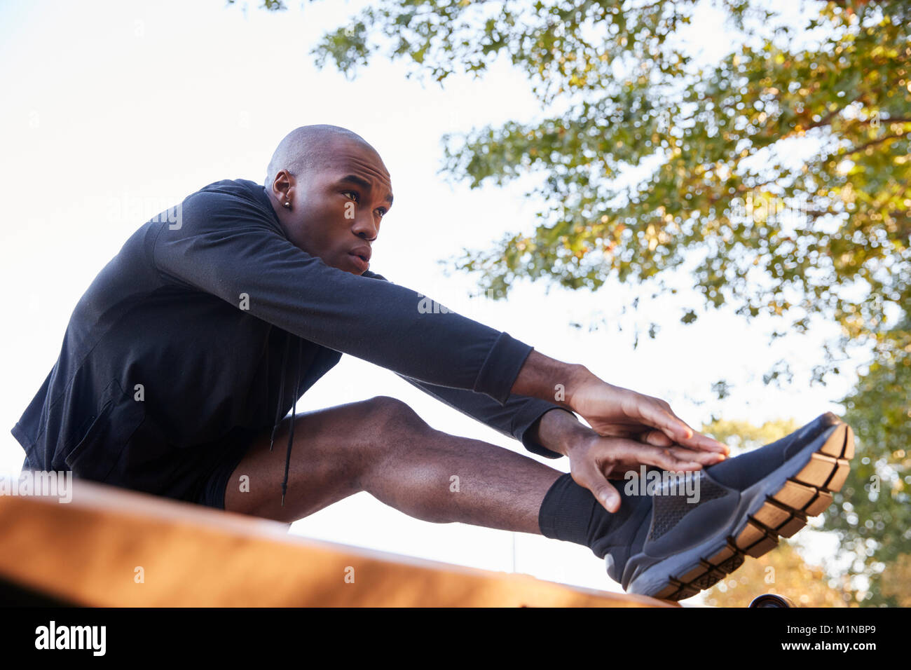Junge schwarze Mann stretching Bein auf einer Bank im Park, in der Nähe Stockfoto