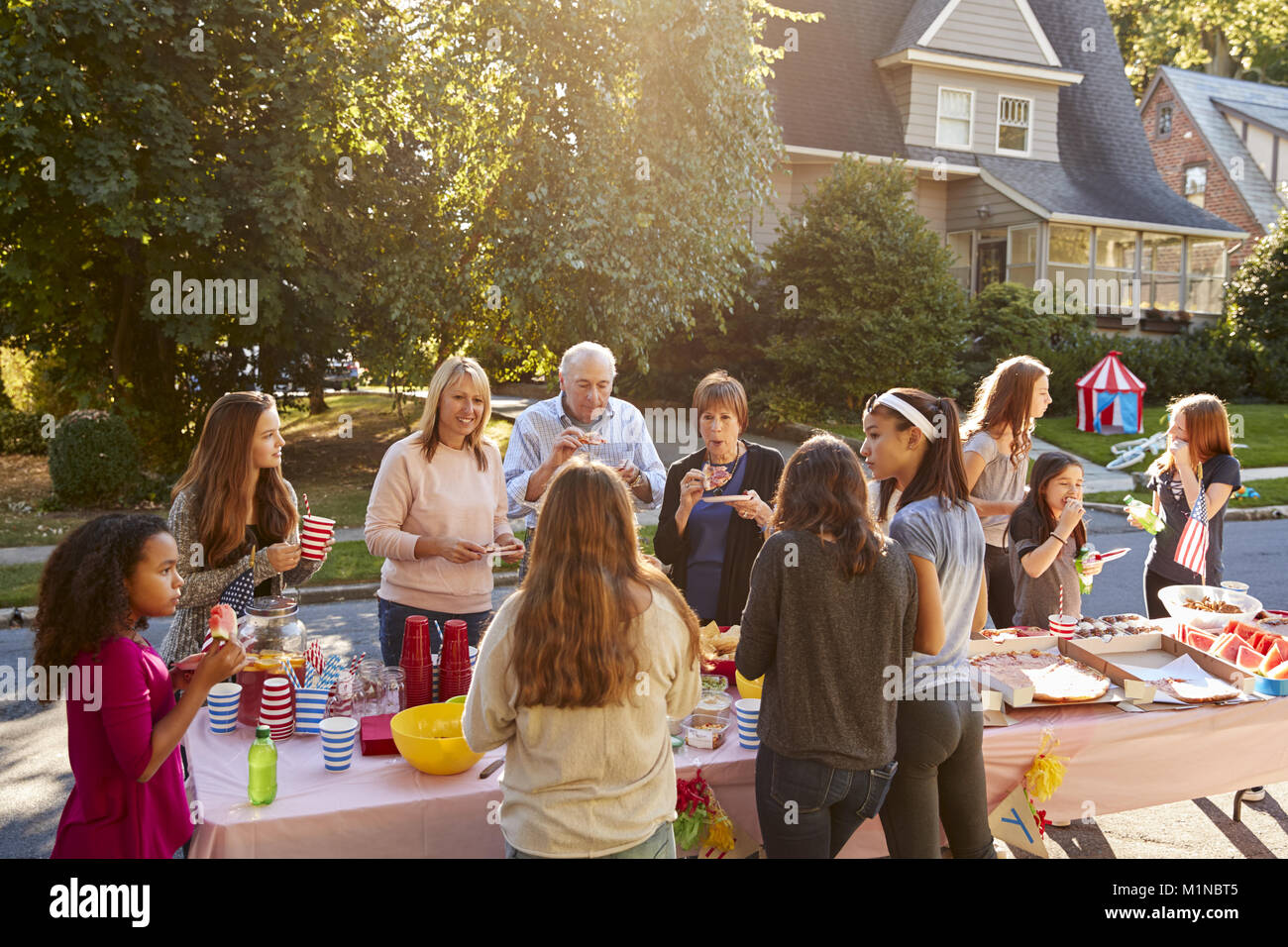 Nachbarn sprechen und Essen rund um einen Tisch in einem Block Party Stockfoto