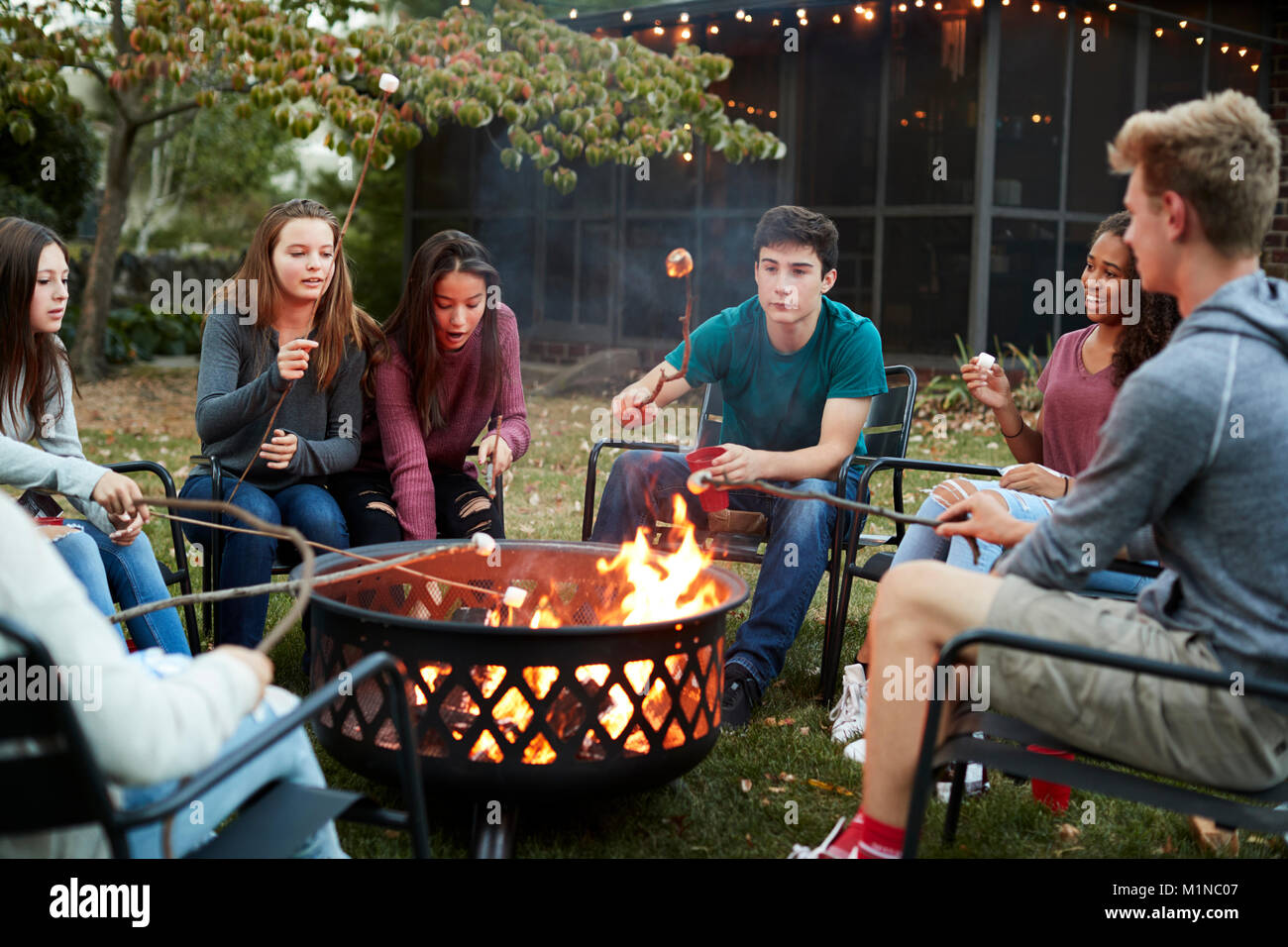 Teenage Freunde sitzen rund um ein Lagerfeuer toasten Marshmallows Stockfoto