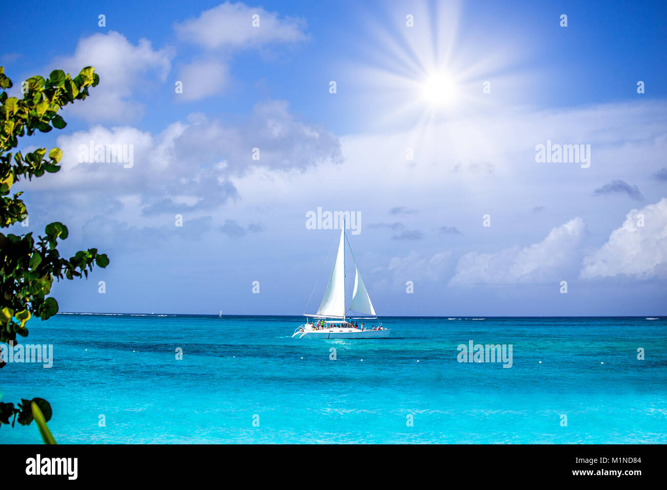 Ein kleines, weißes Segelboot mit Menschen an Bord, crusing auf einem Aqua Ocean unter einem bewölkten Himmel am Nachmittag Stockfoto