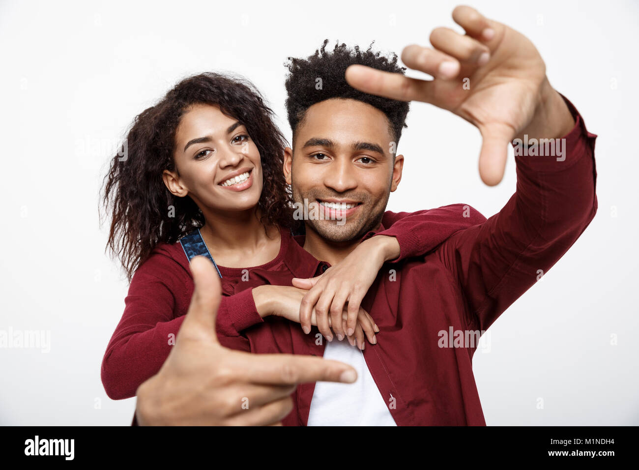 Glückliche junge afrikanische amerikanische Paar durch einen Finger Rahmen und lächelnd beim Stehen auf weißen isoliert. Stockfoto