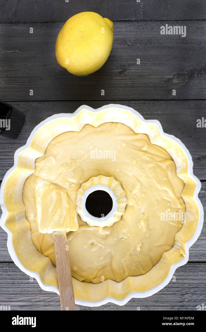 Zubereitung von Teig für einen Zitronenkuchen in einem gelben bundt Wanne mit einem Spachtel auf einer rustikalen Tisch Stockfoto