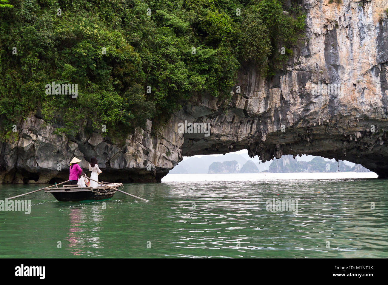 Junge Frauen auf einem Ruderboot außerhalb einer Höhle in der Halong Bay, Vietnam posieren. Die kleinen Inseln und Kalkfelsen Formationen haben sich von der UNESCO zum geschützten Bereich. Stockfoto