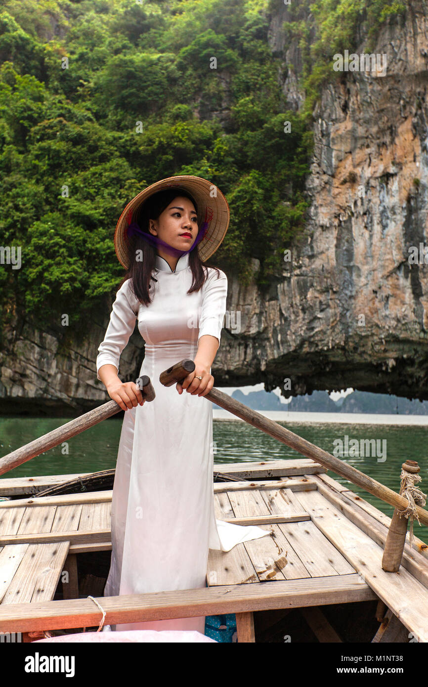Junge Frau mit Ao Dai posieren auf einem Ruderboot in der Halong Bay, Vietnam. Die kleinen Inseln und Kalkfelsen Formationen haben sich von der UNESCO zum geschützten Bereich. Stockfoto
