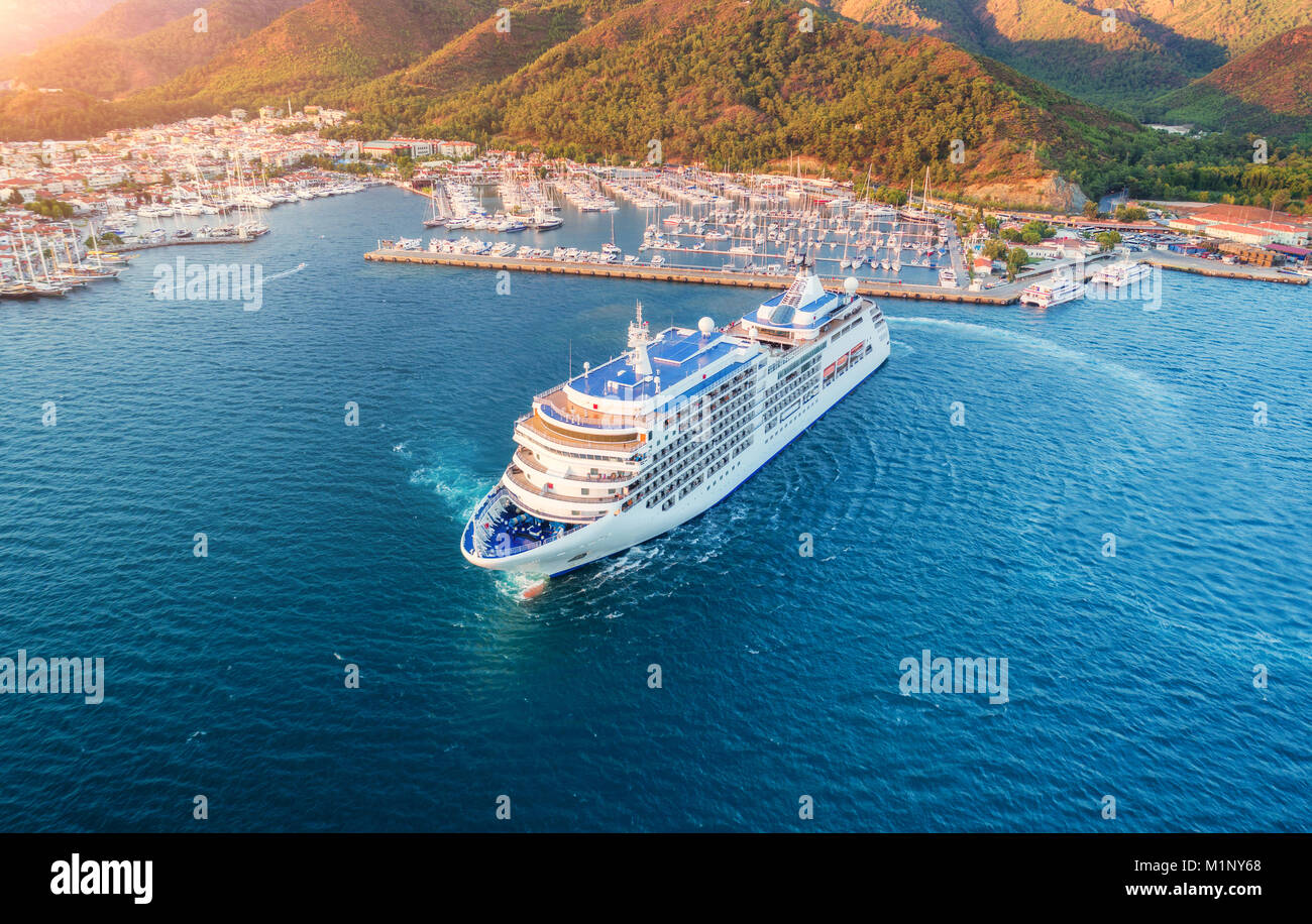 Kreuzfahrtschiff im Hafen. Luftaufnahme der schöne große weiße Schiff bei Sonnenuntergang. Bunte Landschaft mit Yachten in der Marina Bay, Meer, grünen Wald. Ansicht von oben f Stockfoto