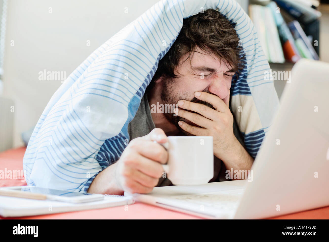 Junger Mann lernt, gähnt, während der Computer im Bett, Home Office, Deutschland Stockfoto