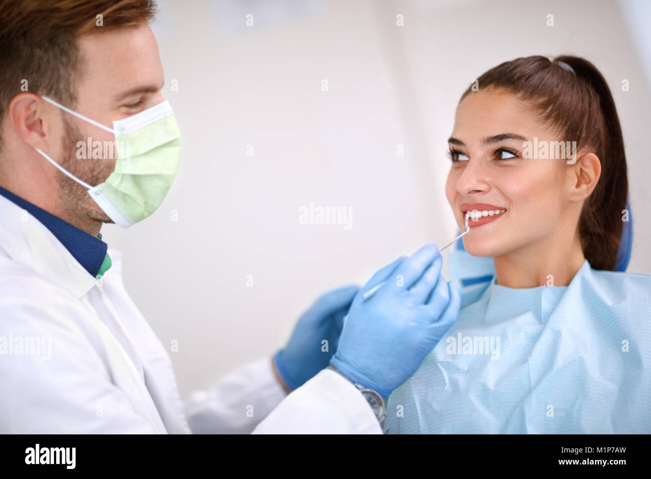 Männliche Zahnarzt untersucht die Zähne der Frau mit Spiegel Stockfoto