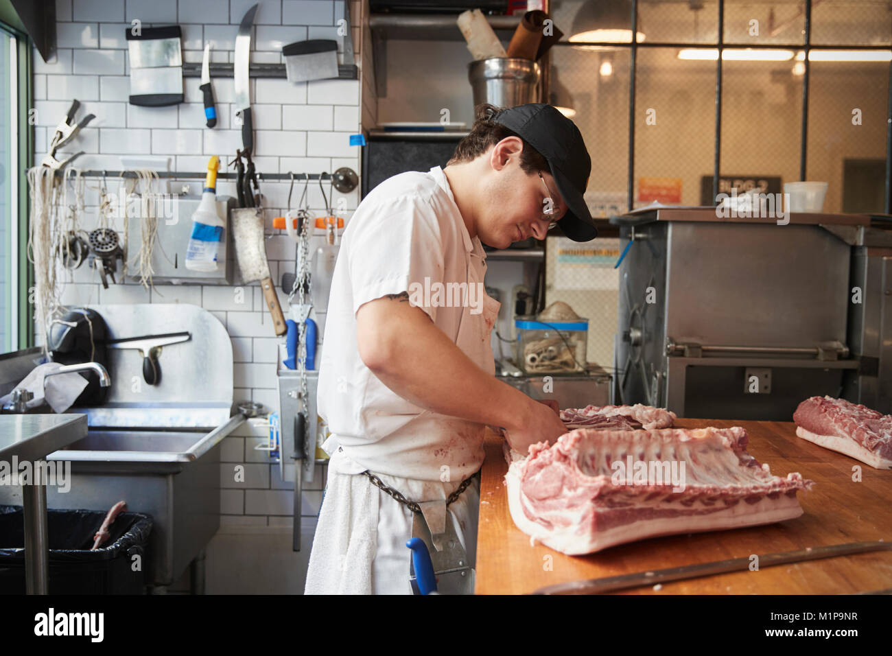 Junge Metzger schneiden von Fleisch in eine Metzgerei zu verkaufen Stockfoto