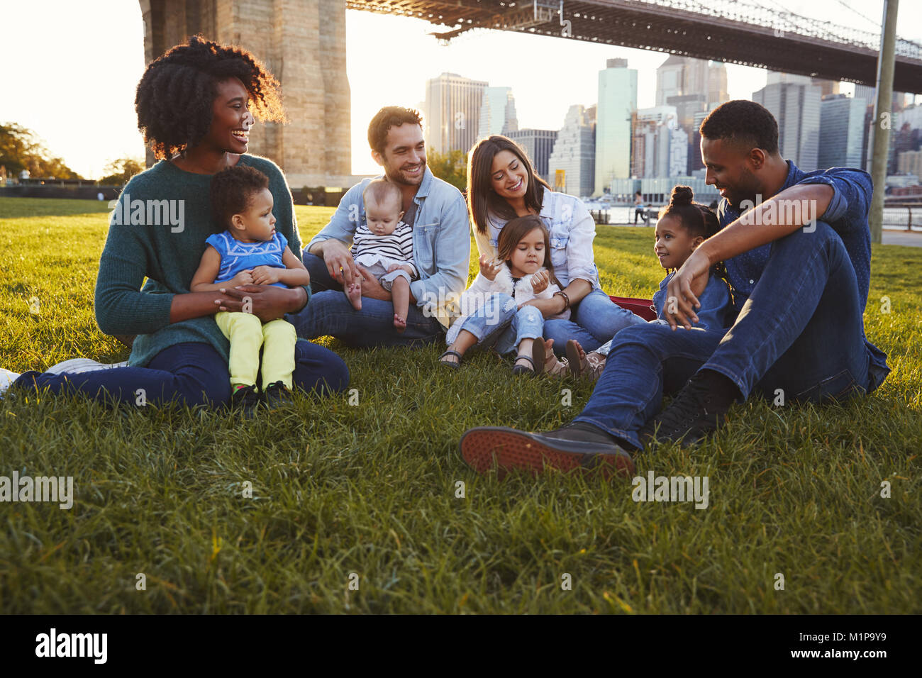 Zwei Familien mit Töchtern sitzen auf Rasen Stockfoto