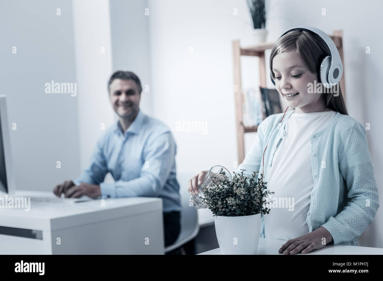 Fröhliche junge Dame Blumen gießen während Vater arbeiten Stockfoto