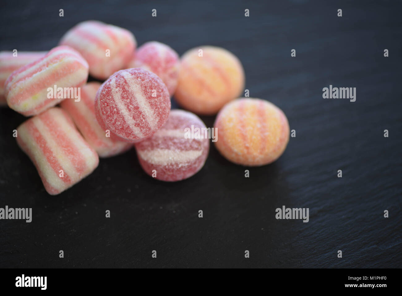Essen von Süßigkeiten Zucker überzogen behandelt oder Süßigkeiten in Pastelltönen und Streifenmuster auf schwarzem Schiefer Hintergrund mit Platz Stockfoto