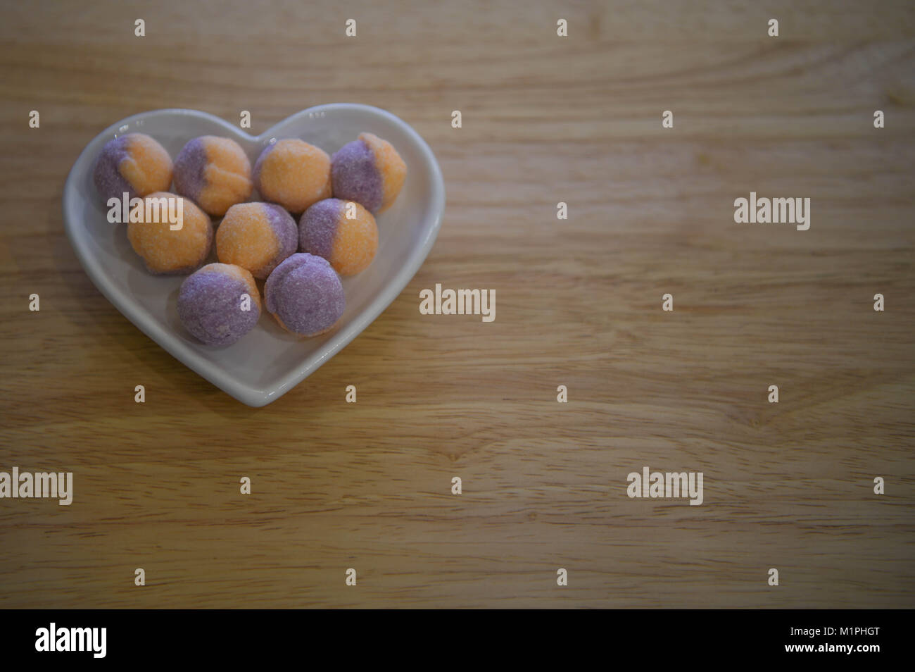Nahrung der traditionellen Süßigkeiten behandelt oder Bonbons in einer Liebe Herzform Teller auf natürlichem Holz und in Orange und Lila Farben mit Fruchtaromen. Stockfoto
