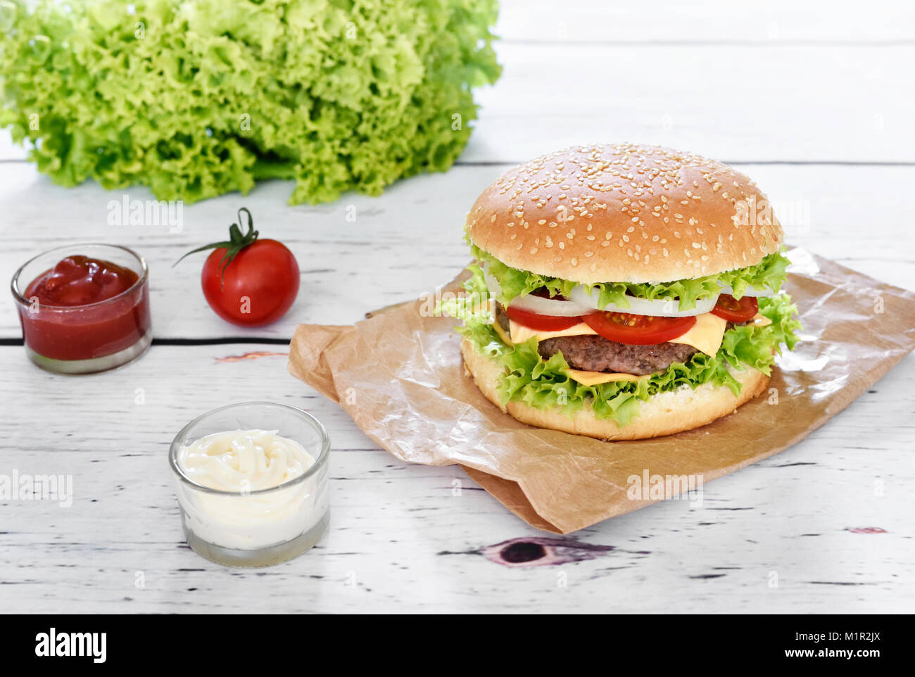 Gourmet Burger mit Soßen auf einem weißen Tisch. Hamburger oder Cheeseburger mit frischen Tomaten, Kopfsalat und Rindfleisch Patty, Fast food Hintergrund. Stockfoto