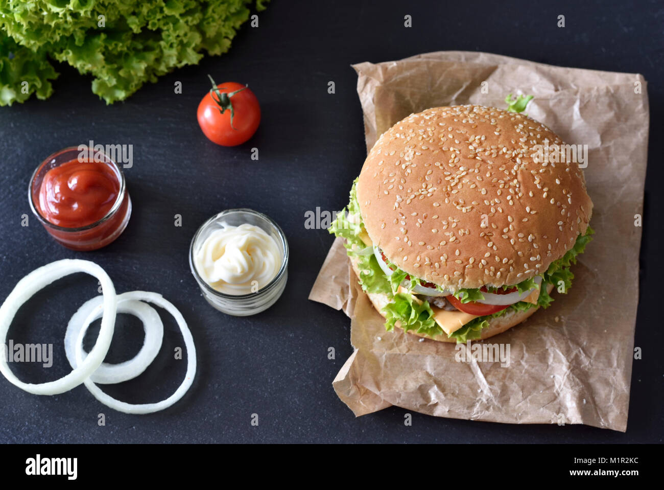 Frische Hamburger, Burger oder Cheeseburger mit Ketchup und Mayonnaise, Zwiebeln und Salat. Leckere Burger auf einer Schiefertafel Platte. Fast food Hintergrund. Stockfoto