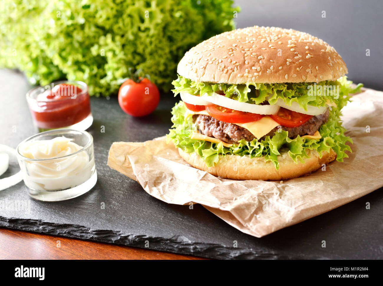 Frische Hamburger, Burger oder Cheeseburger mit Ketchup und Mayonnaise, Zwiebeln und Salat. Leckere Burger auf einer Schiefertafel Platte. Fast food Hintergrund. Stockfoto