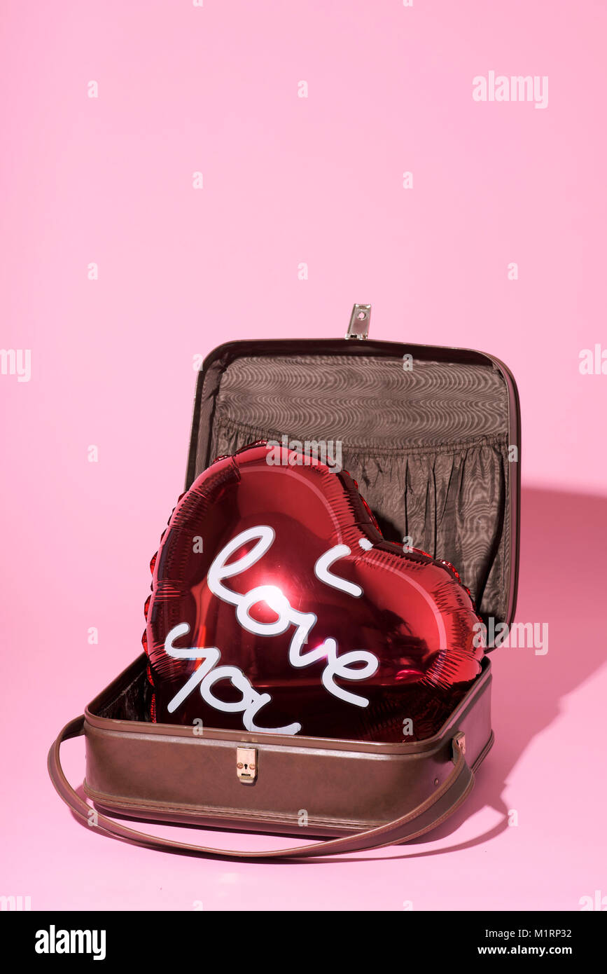 Eine rote herzförmige Ballons mit dem Text "Ich liebe Dich in Es geschrieben, in einem alten Koffer, gegen einen rosa Hintergrund, mit einigen leeren Raum auf der Oberseite Stockfoto