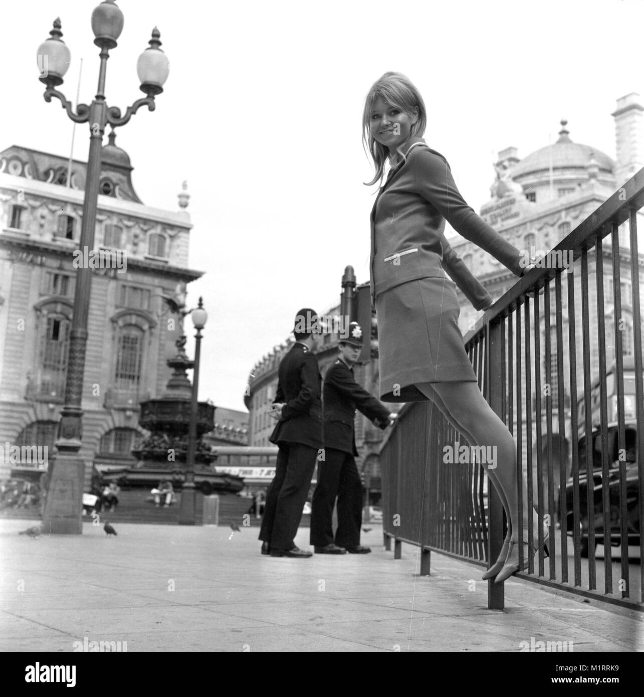 Ein Modell stellt in einem zweiteiligen Rock und Jacke im Freien im Londoner Piccadillyby zwei Polizisten patrouillieren in ca. 1968 tragen eine bunte mini-kleid. Foto von Tony Henshaw Stockfoto