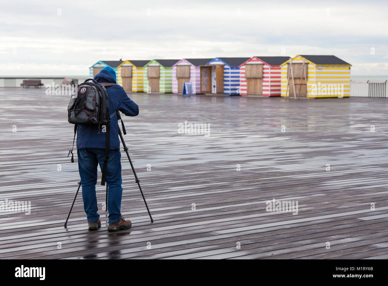 Ein Mann mit einem Stativ nimmt ein Bild von der Hastings Strand Hütten am Pier von Hastings, East Sussex, Großbritannien Stockfoto